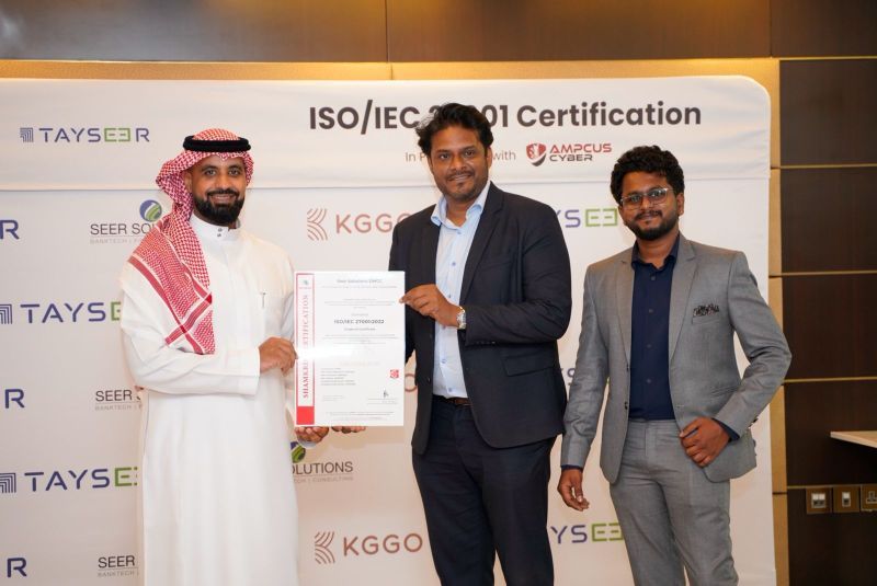 Certificate handover at a branded backdrop reading ISO/IEC 27001 certification in partnership with Ampcus Cyber.